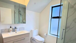 Un baño moderno con cabina de ducha de vidrio, inodoro y tocador con cajones.