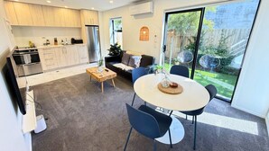 Una cocina moderna con electrodomésticos integrados, un comedor con una mesa redonda y sillas, y un puerta corrediza de vidrio que da a un jardín.