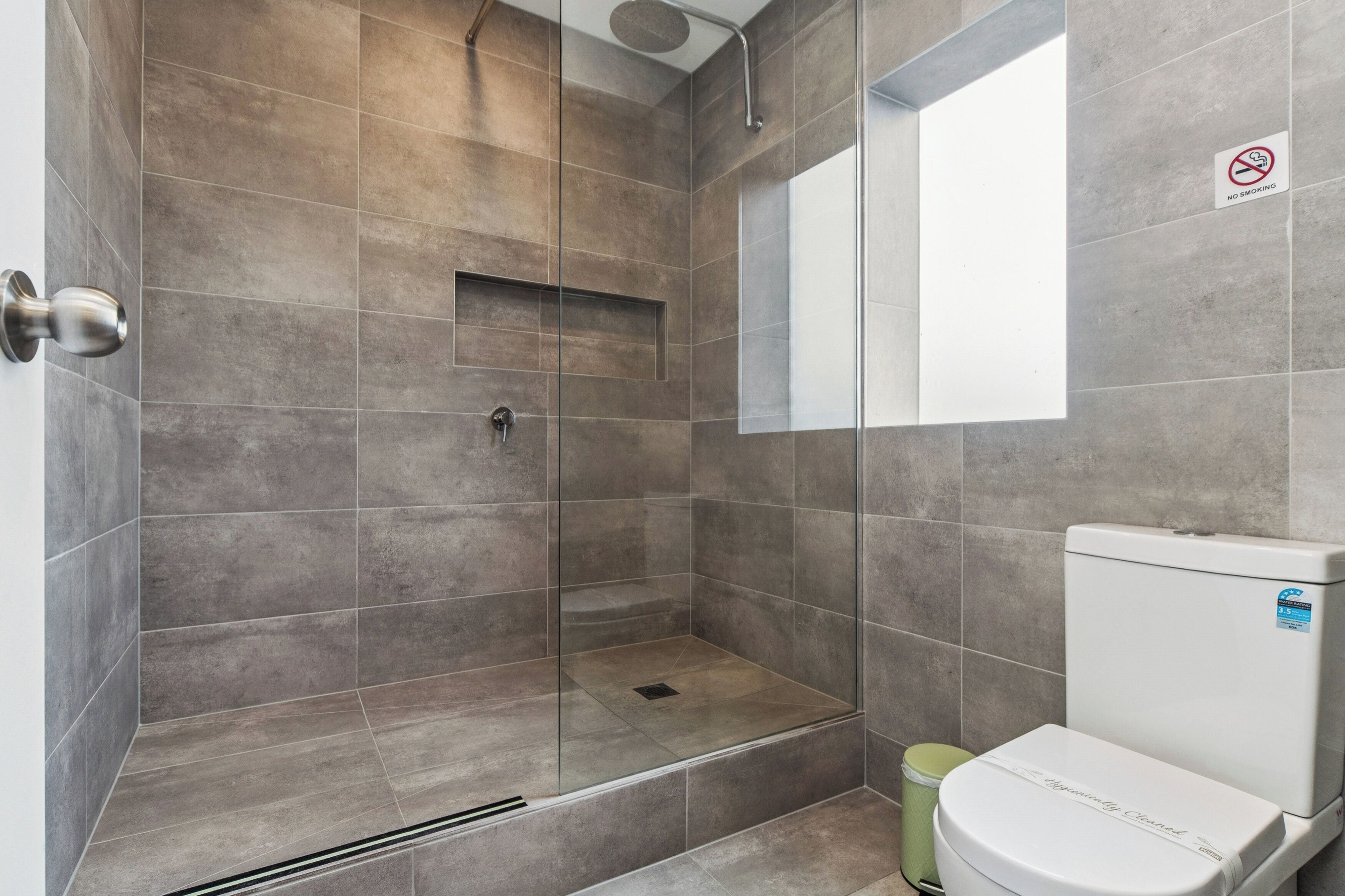 A modern bathroom with a glass-enclosed shower, a toilet, and a 'No Smoking' sign.