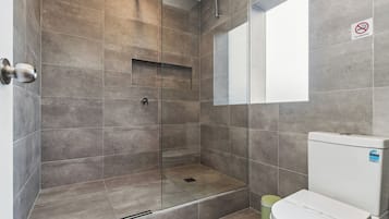 A modern bathroom with a glass-enclosed shower, a toilet, and a 'No Smoking' sign.