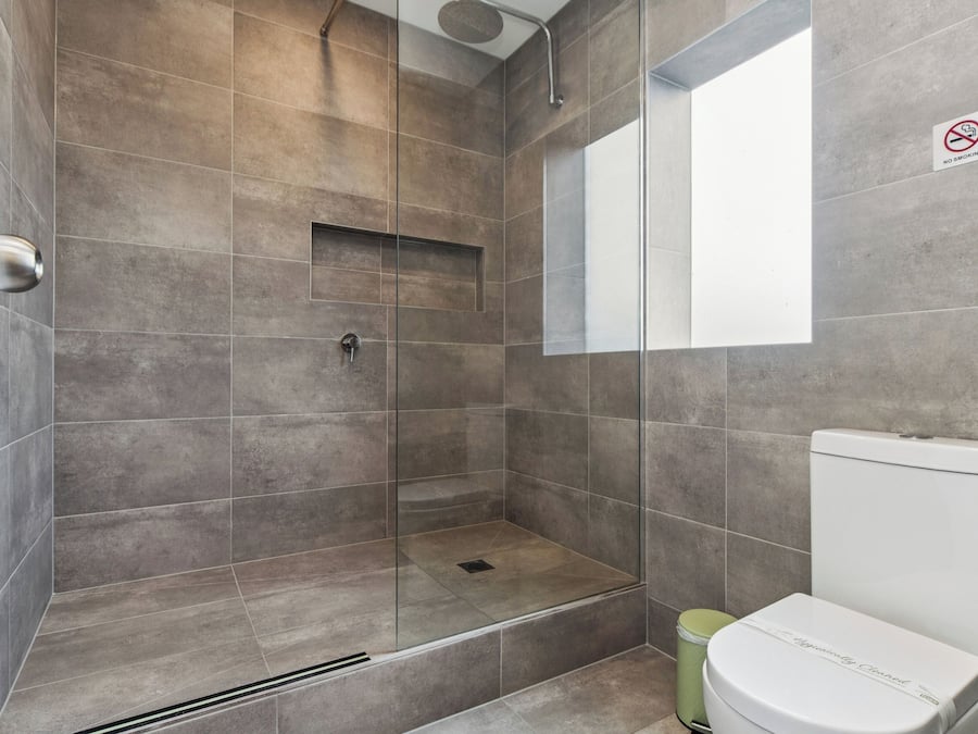 A modern bathroom with a glass-enclosed shower, a toilet, and a 'No Smoking' sign.