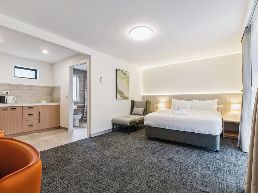 A hotel room with a bed, a desk, a chair, a microwave, and a small kitchen area.