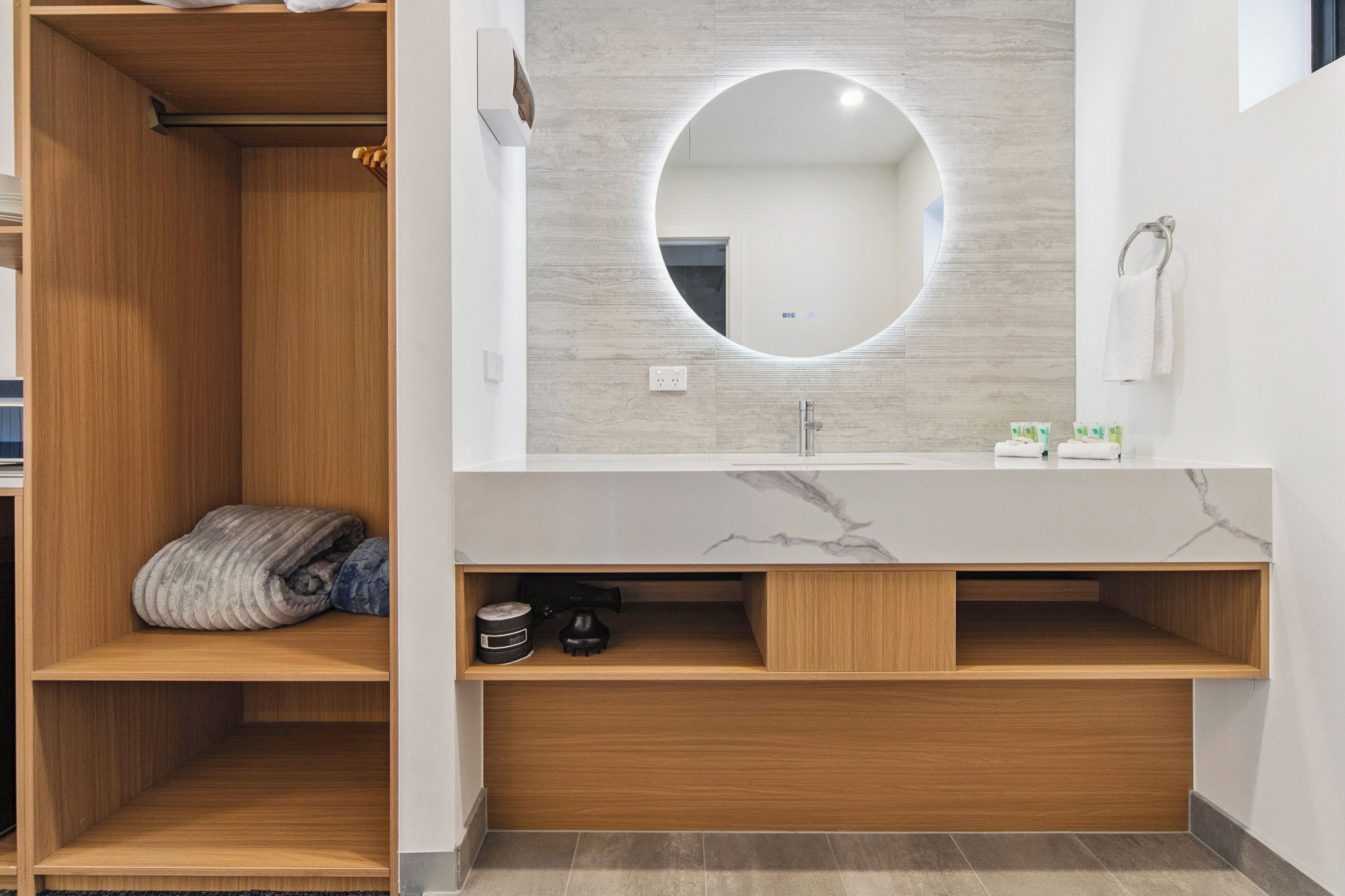 A modern bathroom with a wooden vanity, a round mirror, and a marble countertop.