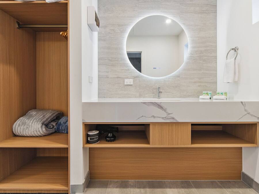 A modern bathroom with a wooden vanity, a round mirror, and a marble countertop.