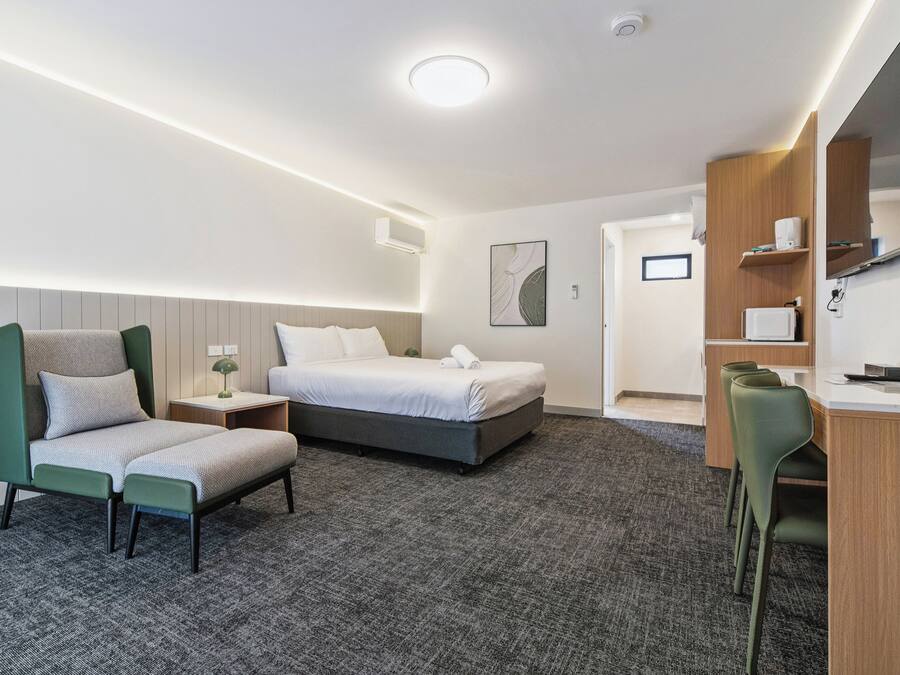 A modern hotel room with a bed, a desk, a chair, and a television.