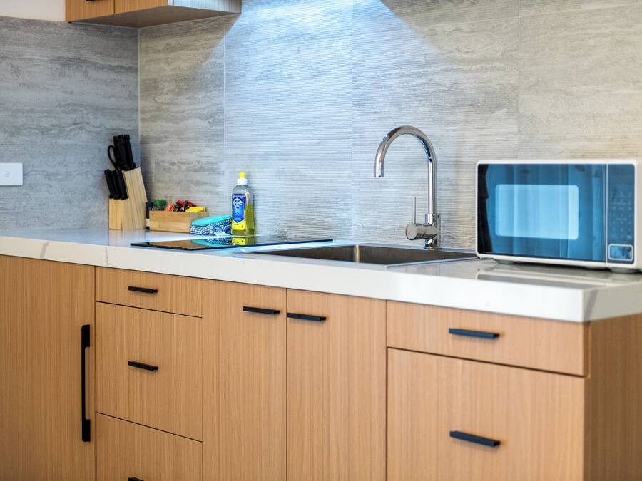 Una cocina moderna con microondas integrado, un lavamanos y armarios de madera.