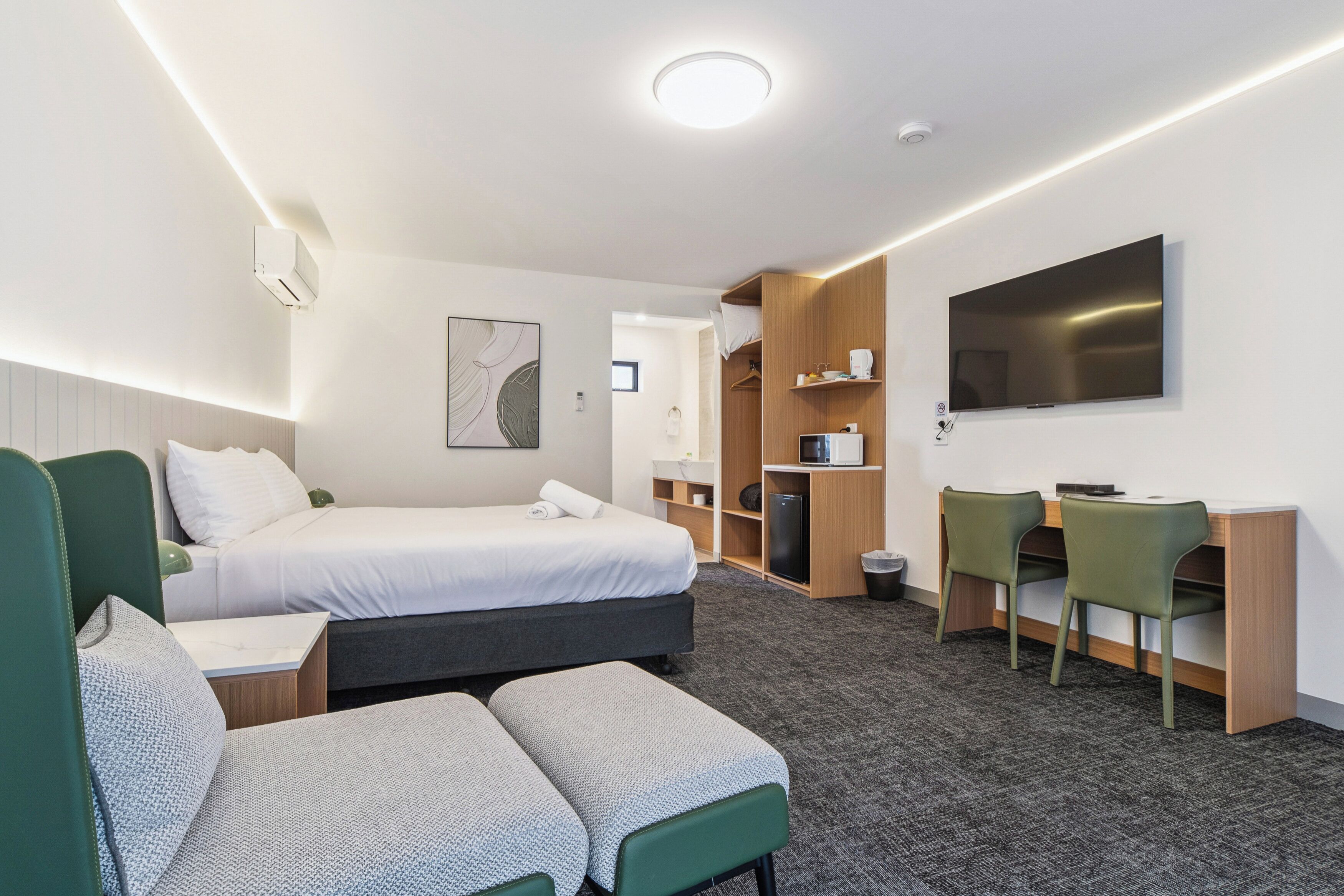 A hotel room with a bed, a desk with chairs, a TV, and a small kitchenette.