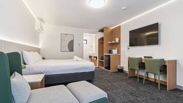 A hotel room with a bed, a desk with chairs, a TV, and a small kitchenette.