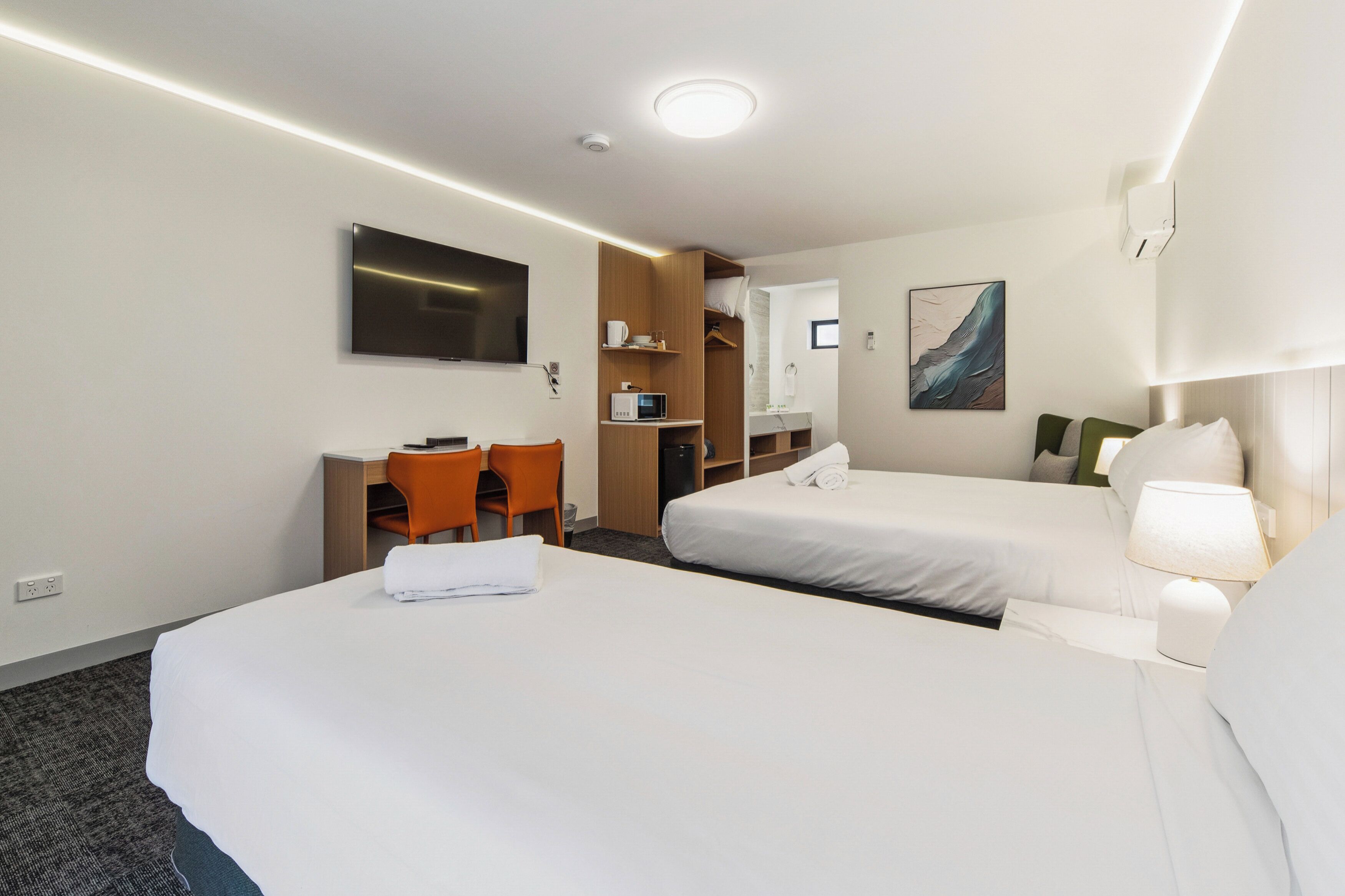 Habitación de hotel con dos camas, un escritorio, una silla, un televisor, un microondas y un cuadro en la pared.