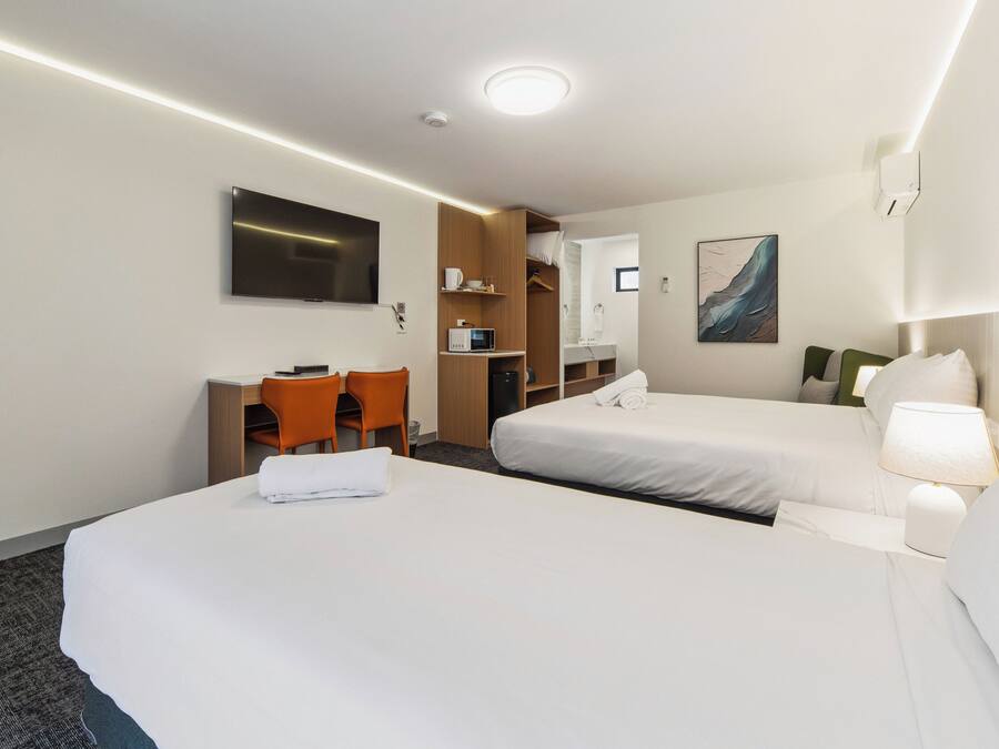Habitación de hotel con dos camas, un escritorio, una silla, un televisor, un microondas y un cuadro en la pared.