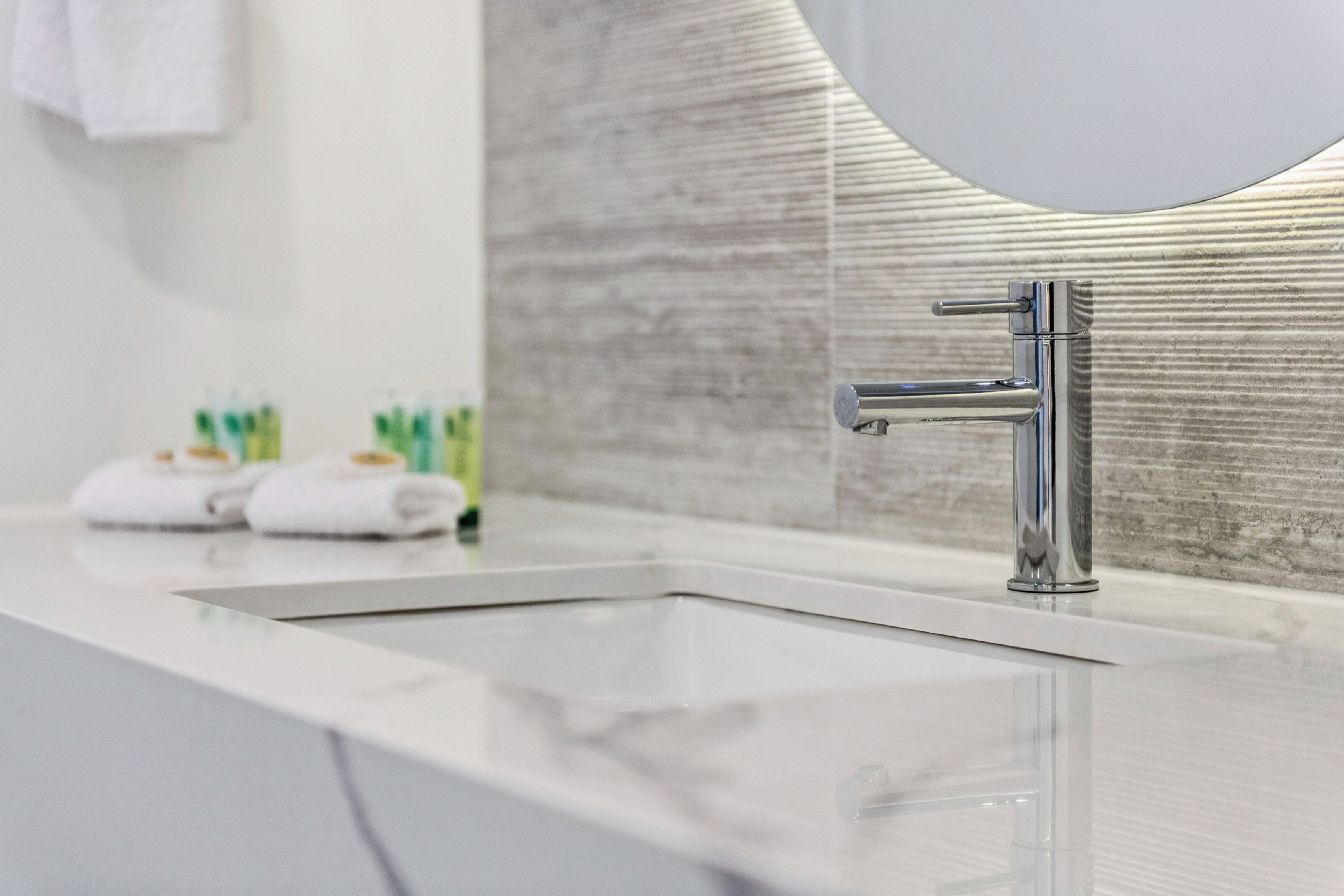 A modern bathroom with a chrome faucet, a white sink, and a large mirror.