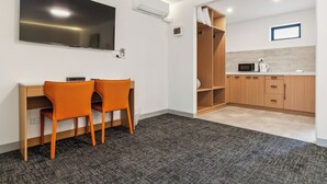 Habitación moderna con escritorio, dos sillas, televisión de pantalla plana, aire acondicionado, microondas y una pequeña kitchenette.