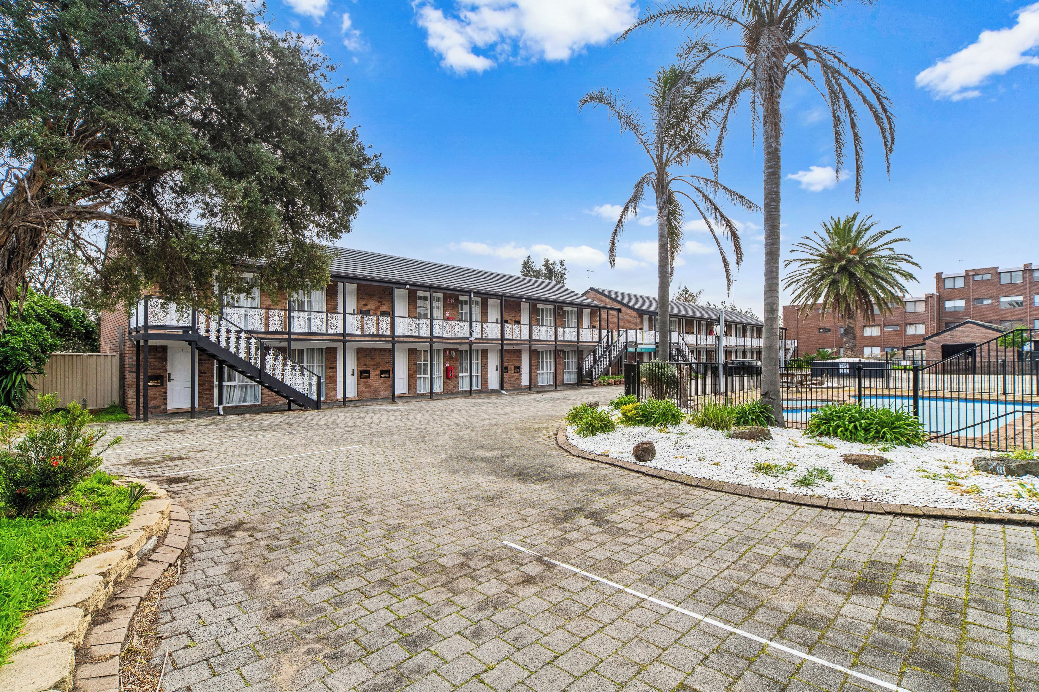 A building with a brick facade, a covered outdoor area with a pool, and a staircase leading to the entrance.