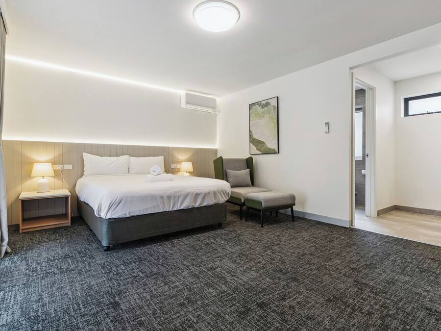 Een hotelkamer met een bed, nachtkastjes, een stoel, een klein tafeltje en een schilderij aan de muur.