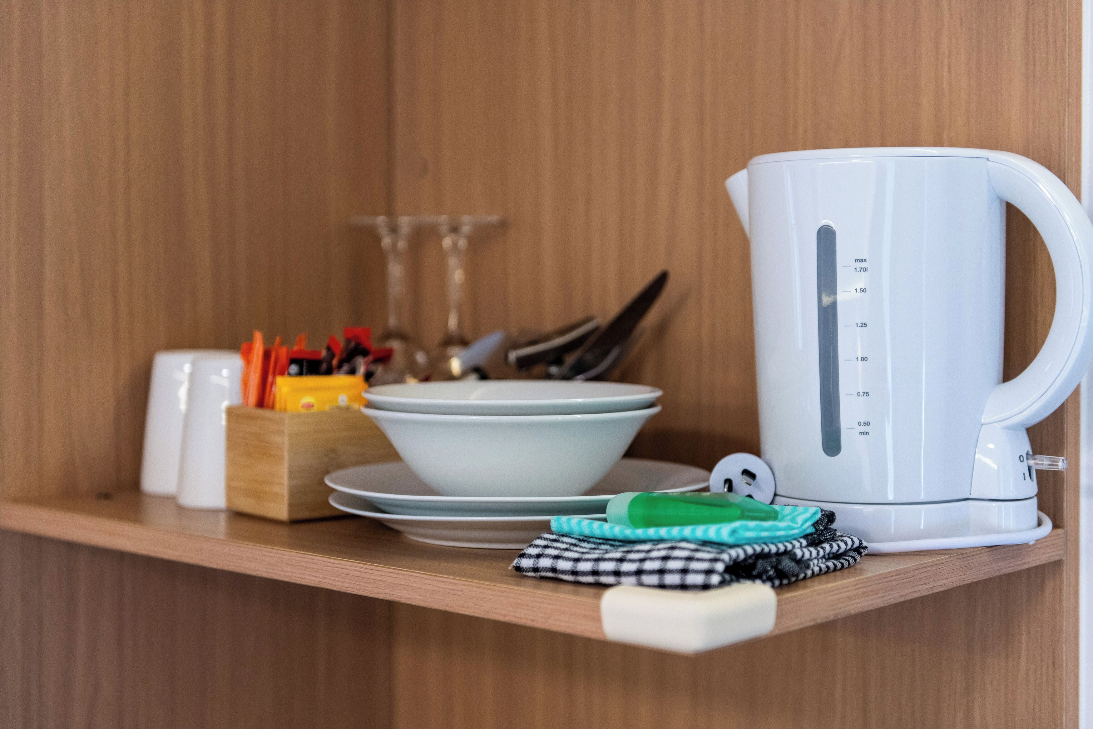 A kitchen shelf with a white kettle, bowls, a knife block, and a dish soap bottle.