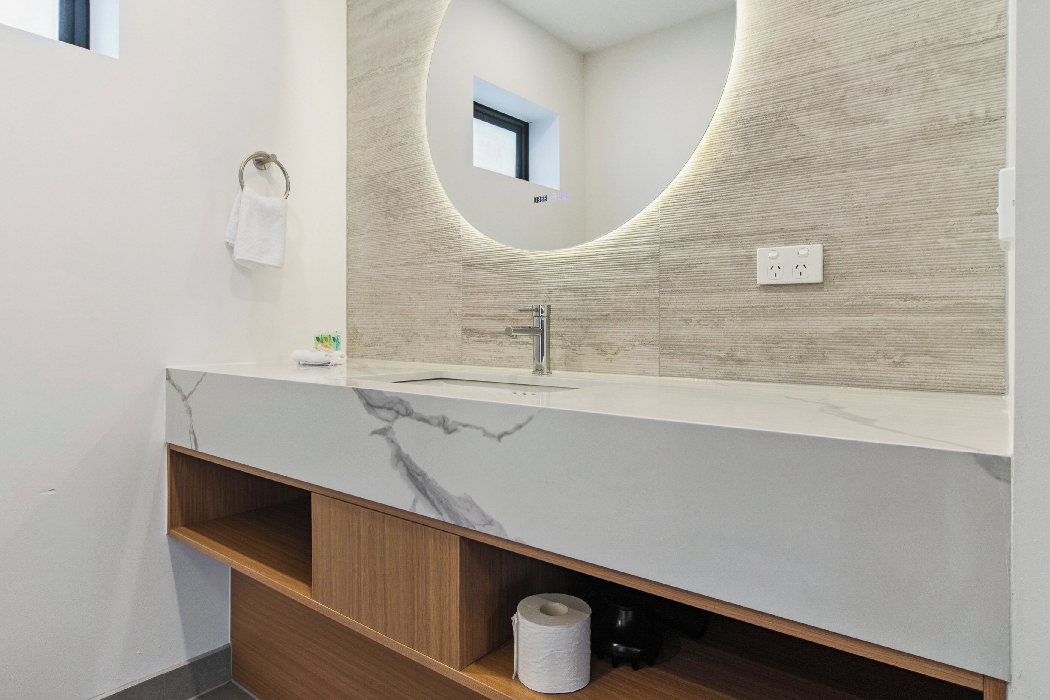 A modern bathroom with a marble countertop, a sink, a mirror, and a towel rack.