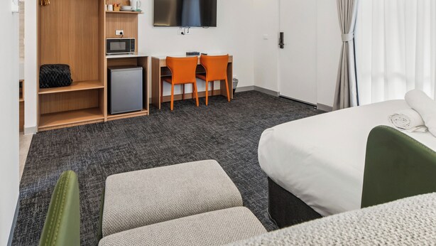 Habitación de hotel con cama, escritorio con dos sillas, televisor, microondas y refrigerador pequeño.