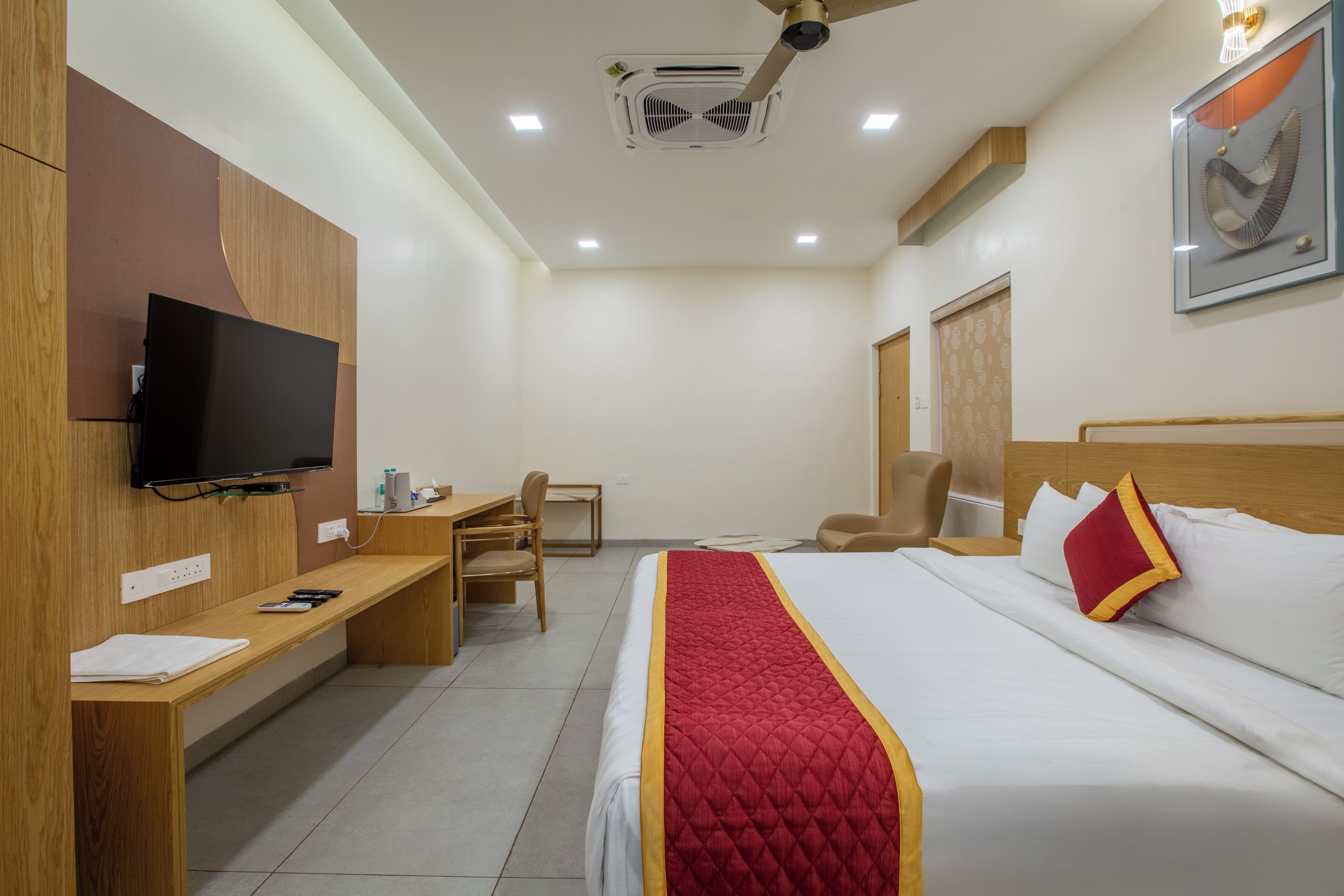 A hotel room with a bed, a desk, a chair, a television, and a ceiling fan.