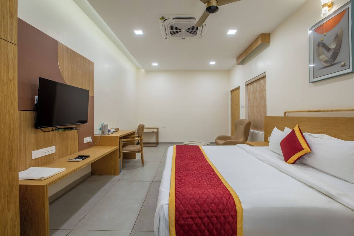 A hotel room with a bed, a desk, a chair, a television, and a ceiling fan.
