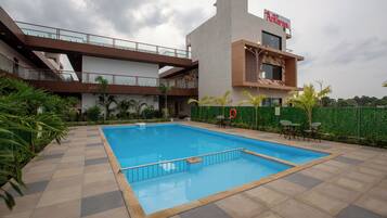 Un edificio moderno con piscina, asientos exteriores y valla verde.