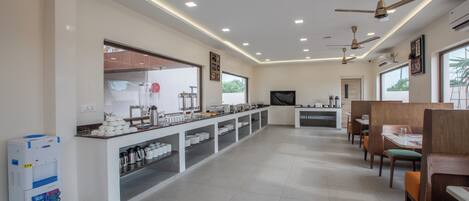 A spacious hotel dining area with a long counter, multiple ceiling fans, and a water dispenser.