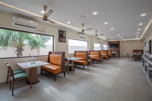 A restaurant with multiple tables and chairs, ceiling fans, and air conditioning units. - La Antaraa  (Tiruchendur)