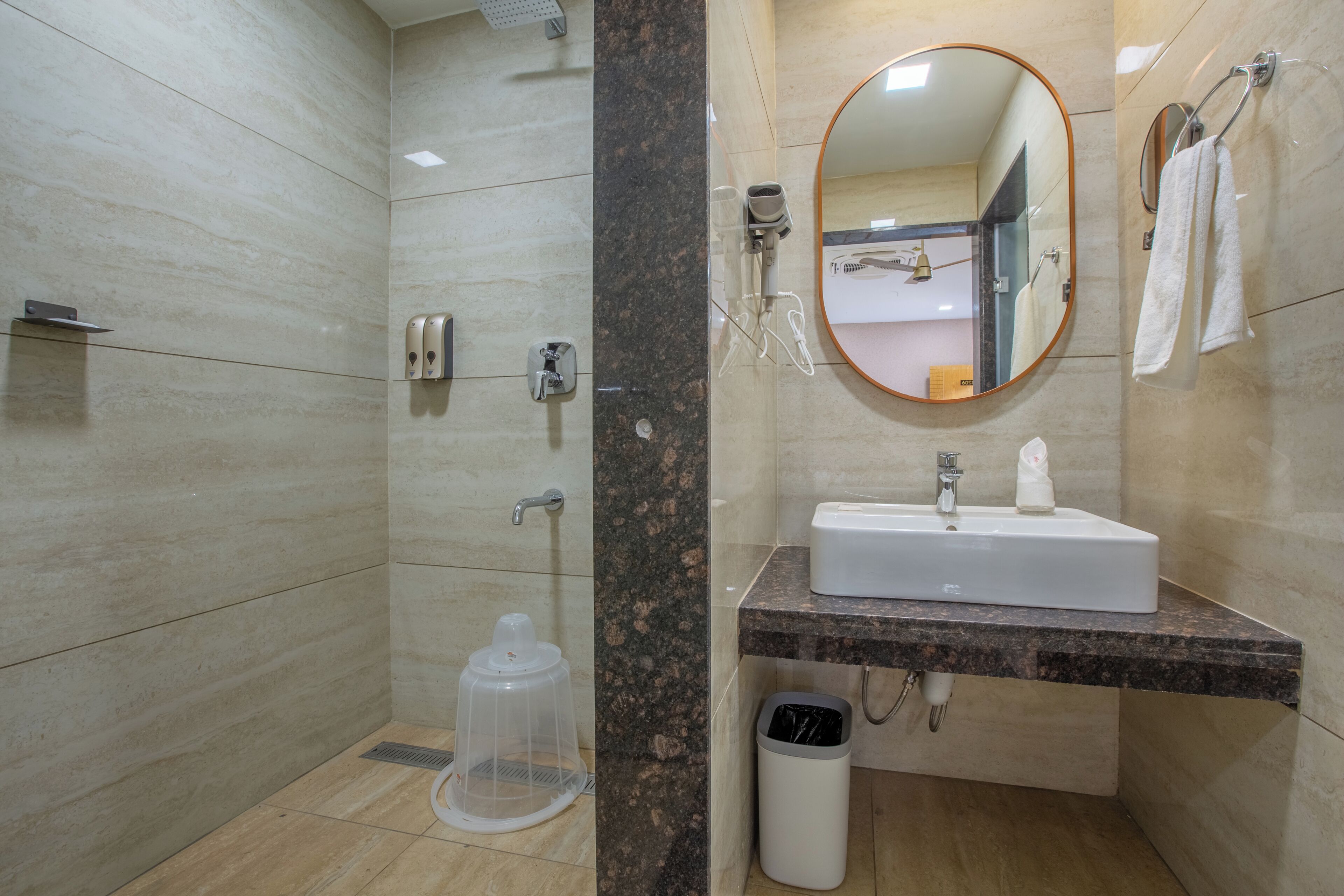 Ein modernes Badezimmer mit Dusche, Waschbecken, Spiegel, Handtuchhalter und Mülleimer.