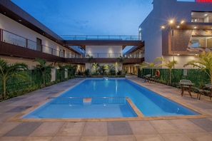 A swimming pool with a surrounding deck, a covered walkway, and a building with a modern design.