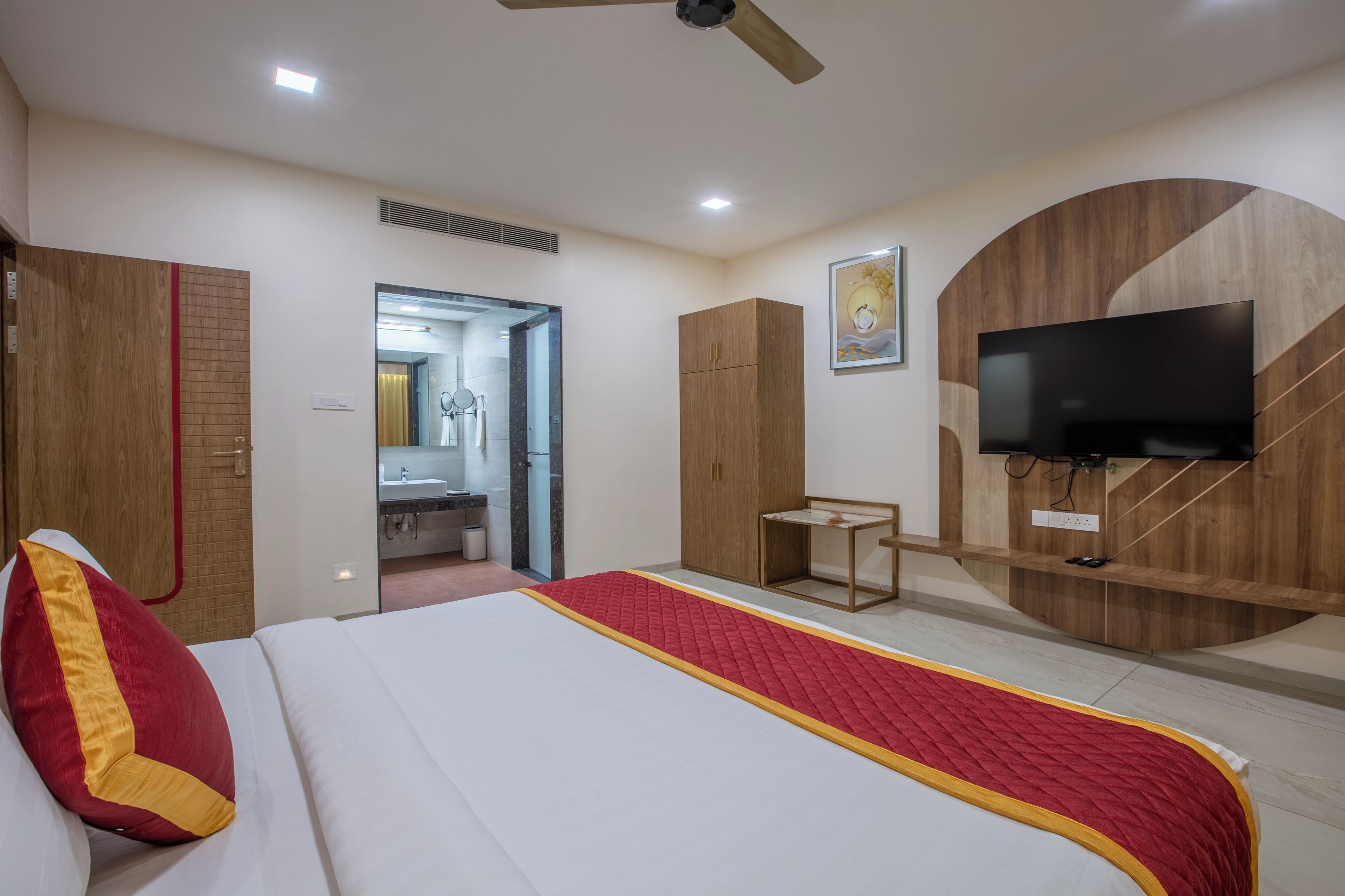 A hotel room with a bed, a TV, a wardrobe, and a bathroom visible through an open door.