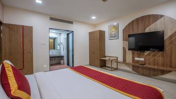 A hotel room with a bed, a TV, a wardrobe, and a bathroom visible through an open door.
