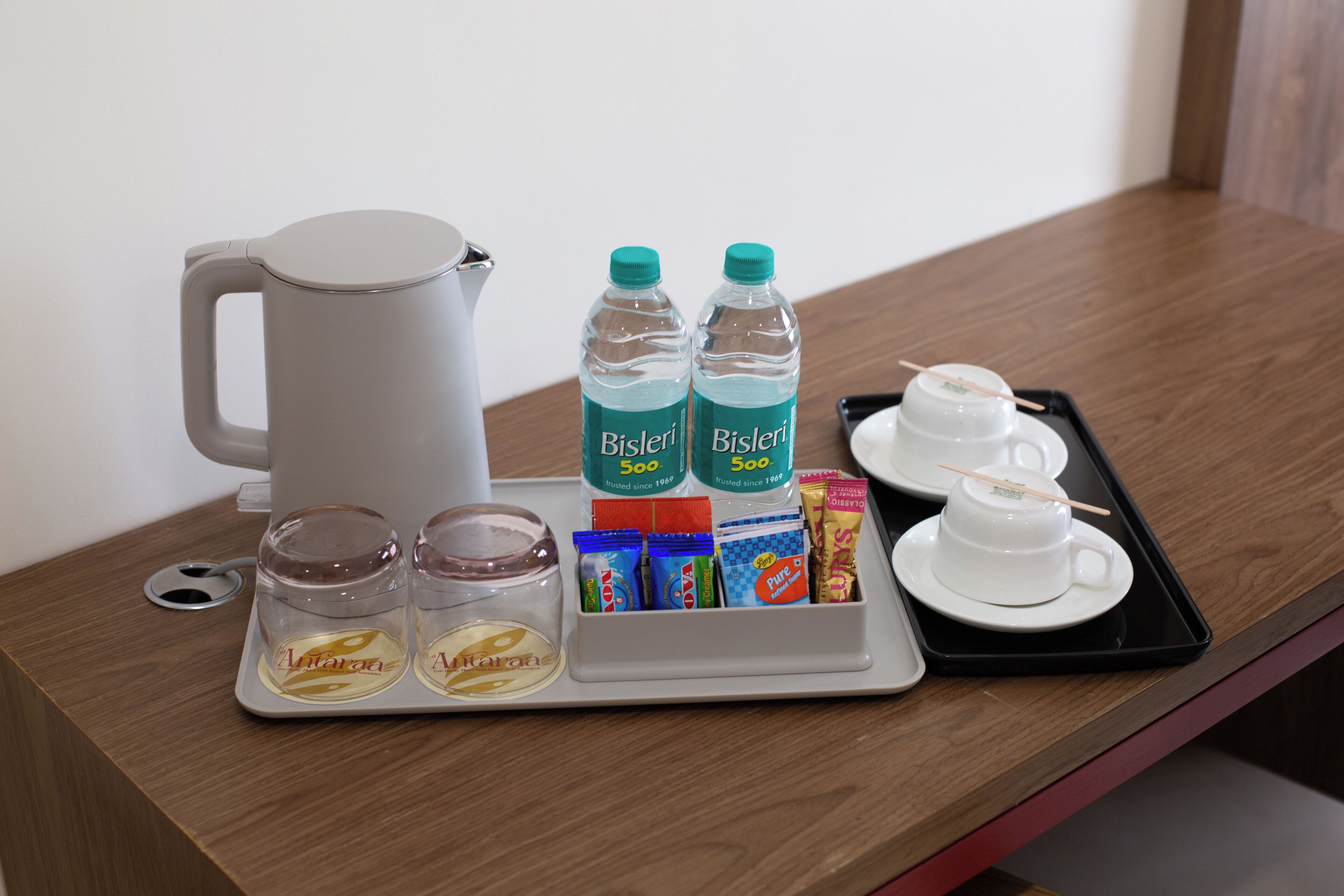 A tray with a coffee maker, water bottles, tea, and snacks on a wooden table.