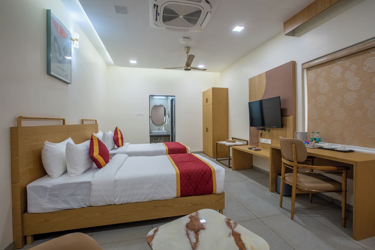 A hotel room with two beds, a desk, a chair, a TV, and a ceiling fan.