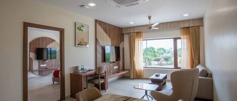 A modern hotel room with a dining area, a TV, a sofa, and a large window.