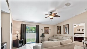 Una sala de estar con ventilador de techo, sofá, mueble para televisión y puerta corrediza de vidrio que da a un patio.