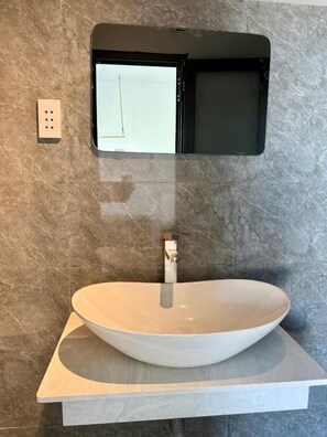 Une salle de bain dotée d’un grand lavabo rond, d’un miroir fixé au mur et d’une prise de courant.
