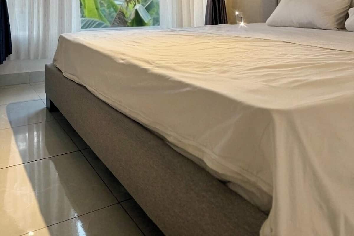 Une chambre à coucher avec un grand lit, des rideaux, une vue sur la verdure et un sol carrelé.