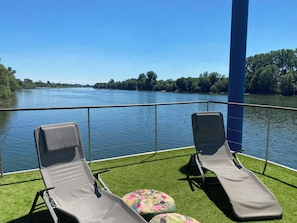 Deux fauteuils confortables sur une terrasse avec vue sur la riviĂšre.