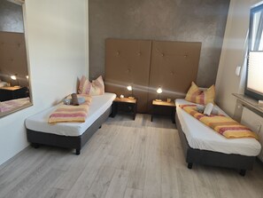 Ein Hotelzimmer mit zwei Betten, einer breiten gepolsterten Kopfteil, Nachttischen mit Lampen und einem Spiegel.