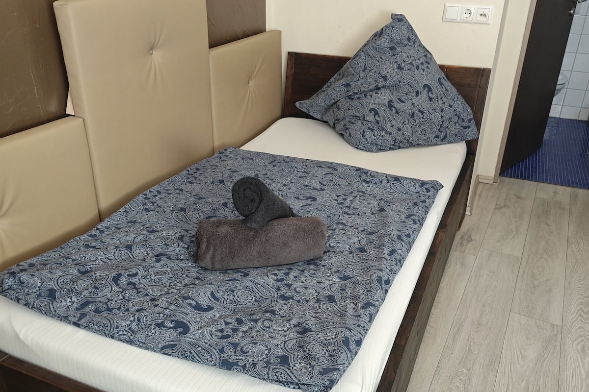 A bed with a patterned bedspread, a rolled towel, and a pillow.