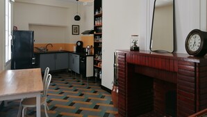 Una cocina con una mesa de madera, sillas, un refrigerador, un reloj y una chimenea de ladrillo.