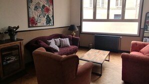Sala de estar con sofá, sillón y mesa de centro. Se ve una ventana con vistas a edificios.