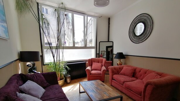 Una sala de estar con un sofá morado, un sofá rojo, una mesa de centro de madera, una planta en maceta y un espejo en la pared.
