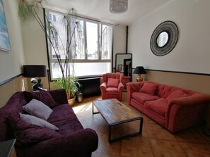 A living room with a purple sofa, a red sofa, a wooden coffee table, a potted plant, and a mirror on the wall. - Charming townhouse in the historic center of Saintes (Saintes)