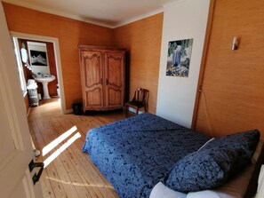 Une chambre à coucher avec une armoire en bois, un lit avec une literie à motifs, une chaise et un tableau accroché au mur.