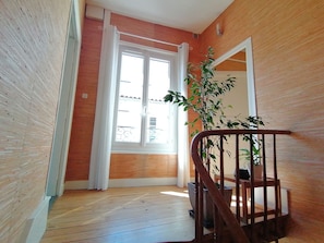 Un couloir au plancher de bois, avec une porte blanche et un escalier doté d’une rampe en bois.