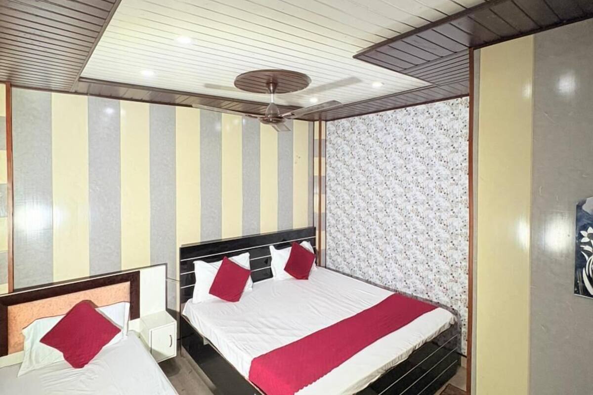 Hotellihuone, jossa on kaksi sänkyä, kattotuuletin, minibaari ja kuvioitu seinä.
