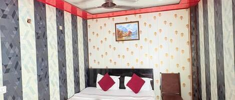 A hotel room with a bed, a chair, a ceiling fan, and a painting on the wall.