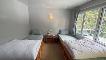 Une chambre avec deux lits simples, une petite table avec une lampe et une fenêtre avec des rideaux.