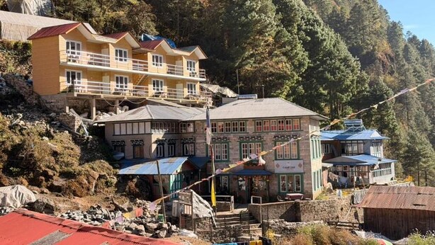 A multi-story building with balconies, a stone facade, and a mountainous backdrop.
