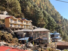 Un edificio de varios pisos con balcones, fachada de piedra y montañas al fondo.